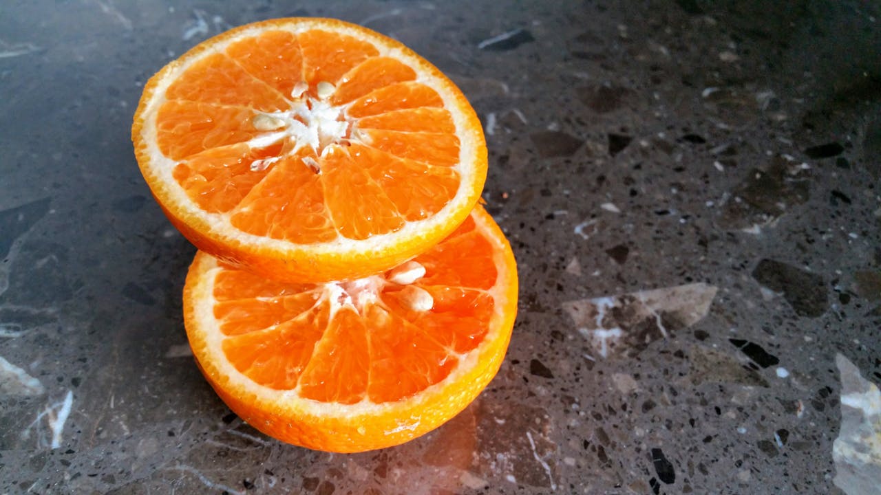 Close-up of two juicy orange slices stacked on a textured marble surface, highlighting their vibrant color.